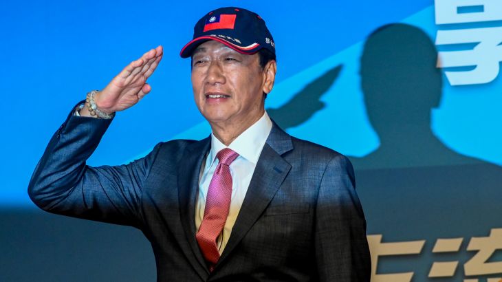 Terry Gou saluting as he announces he will run as an independent in Taiwan's presidential election. He is wearing a baseball cap with the Taiwan flag on it