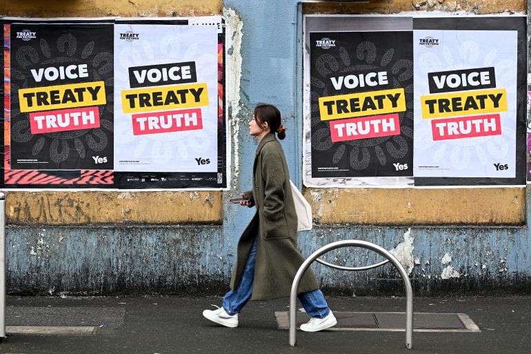 A woman walks past billboards for the 'yes' vote. They read Voice, Treaty, Truth.