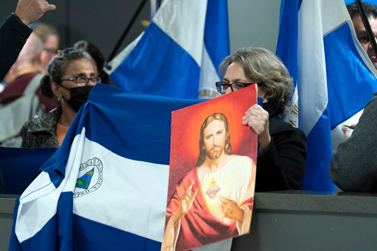 A woman holds up a portrait of Jesus, while another drapes a Nicaraguan flag across the barrier at the arrival gate at an airport in Washington, DC.