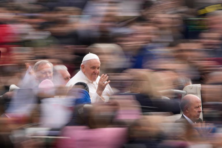 The Pope pictured entering St Peter's Square. The crowd around him is blurred. He is waving and smiling.