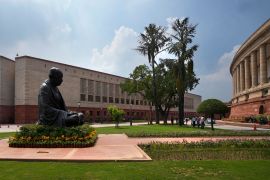 A statue of Mahatma Gandhi sits between the old and new Parliament House buildings on the opening day of the monsoon session of the Indian parliament, in New Delhi, India