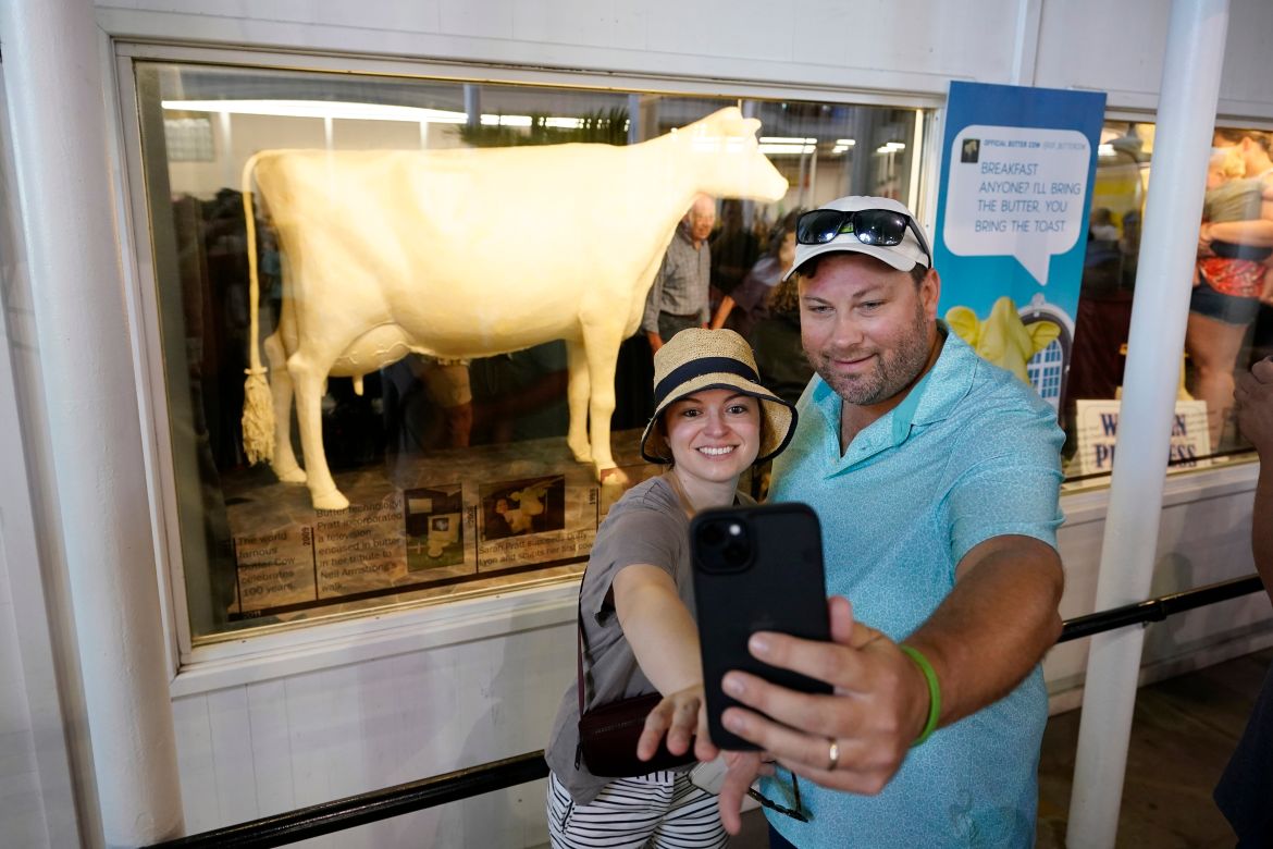 A couple poses for a selfie in front of a cow sculpted from butter.
