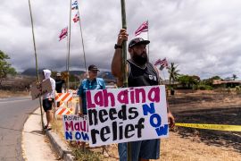 Dustin Pilialoha stands with a sign while waiting for the arrival of President Joe Biden outside the Lahaina Civic Center in Lahaina, Hawaii, Monday, Aug. 21, 2023. His sign reads: "Lahaina needs relief now."