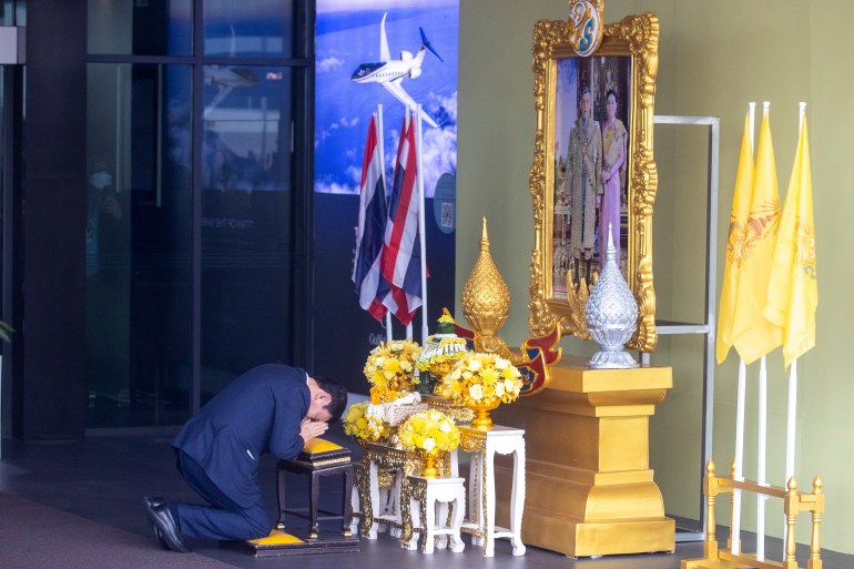 Thaksin kneeling in front of a portrait of the Thai king