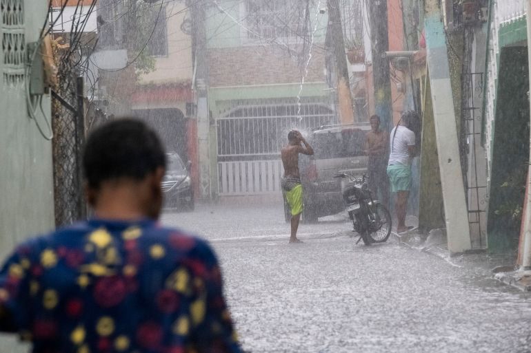 A man stands under a roof drain as rain from Tropical Storm Franklin brings major rainfall to the Dominican Republic