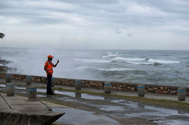 A man takes a photo with his phone as waves crash on the sea wall in Santo Domingo, Dominican Republic
