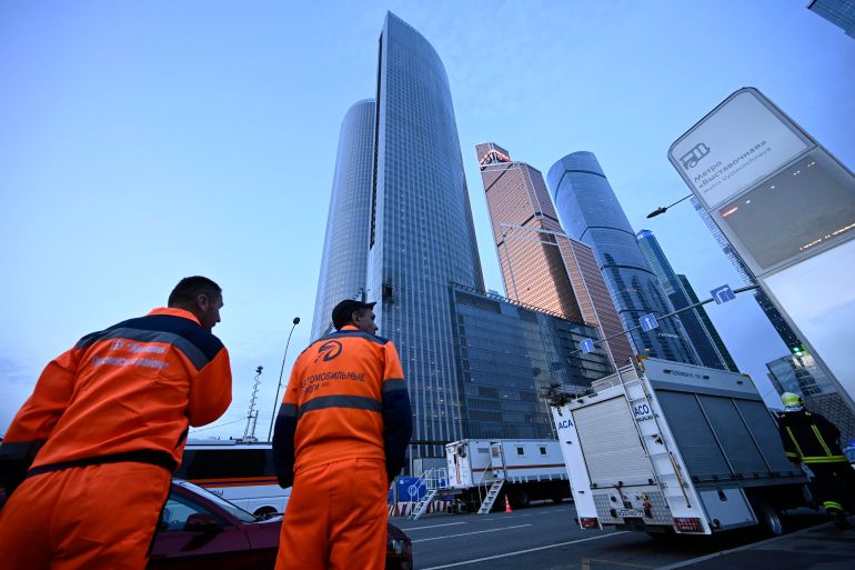 Workers in high-viz suits look up towards skyscrapers after a building under construction in Moscow was hit by a drone