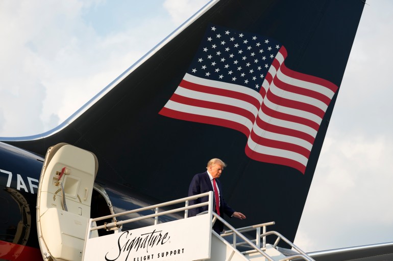 Donald Trump descends a set of stairs connected to the door of his plane, which is emblazoned with an American flag on its tail.