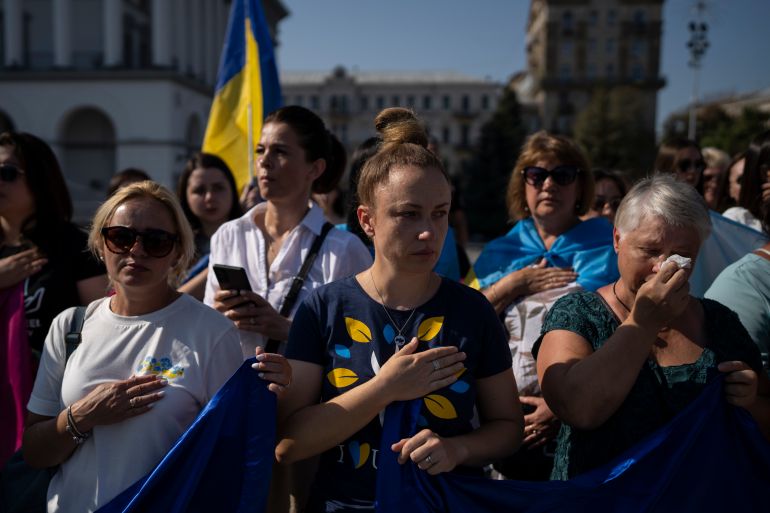 Women crying as they listen to the Ukrainian national anthem at a protest in Kyiv. They are urging the Ukrainian government to do more to bring back their family members who were taken hostage after fighting in Mariupol. They have their hands on their hearts. Some are holding Ukrainian flags