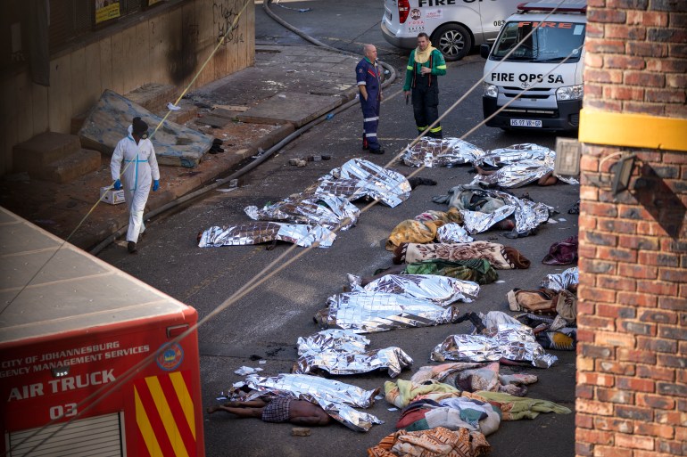 Medics stand by the covered bodies of victims of a deadly blaze in downtown Johannesburg