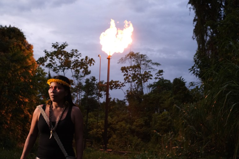 In the twilight, an Indigenous leader stands in front of a gas flare near an oil drilling site.