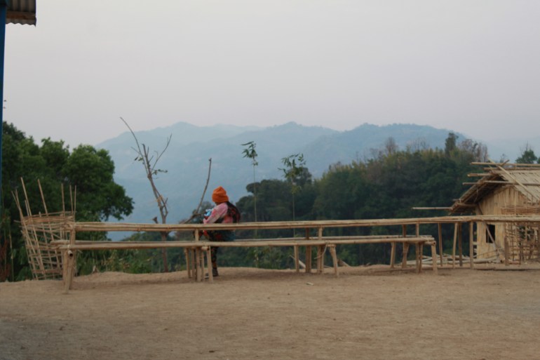 A woman sitting on a long bamboo bench with her baby. She is looking out at a view of tree-covered mountains.