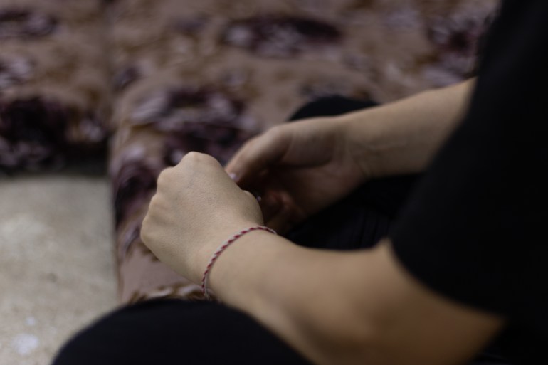 Faqziya's hands as she speaks to Al Jazeera. On her wrist is a white and red twisted thread bracelet.