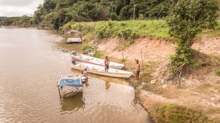 Francisco Juruna, Socorro Juruna and Jardel Juruna stand in the shallow waters of the Xingu River with their canoes.