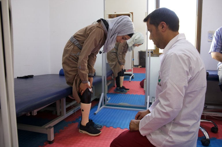 Rima tries on her new leg as her doctor observes