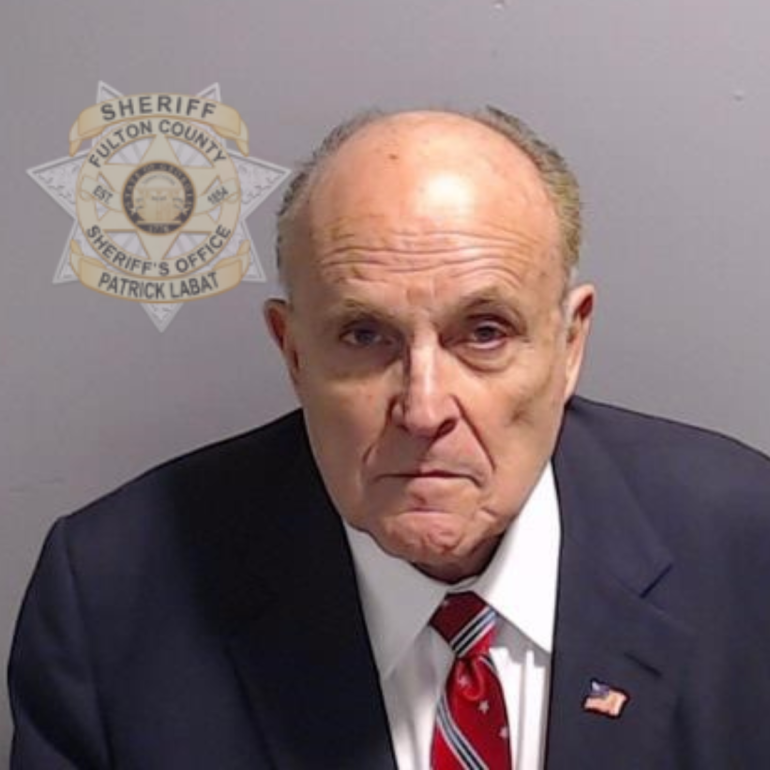 A mugshot of Rudy Giuliani with a seal for Fulton County's Sheriff in the background.