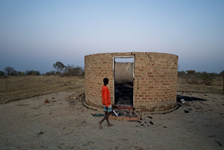 A young boy walks past a neighbour's burnt kitchen in Hanke B Village, Zimbabwe