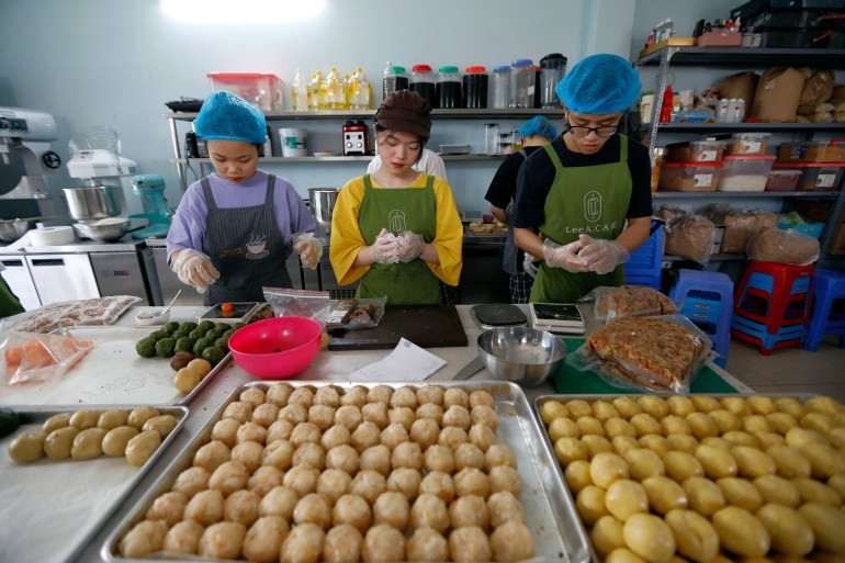 Workers in a bakery in Hanoi prepare mooncakes. The pastries are on a large tray in front of them ready to be shaped.