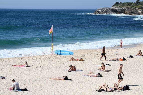 People lying on the beach in Sydney amid a heatwave. The sea is blue and waves are breaking on the sand.