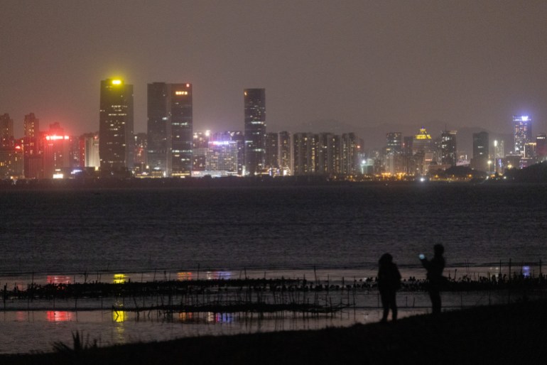 A photo of people standing on the beach against the skyline of Chinese city Xiamen.