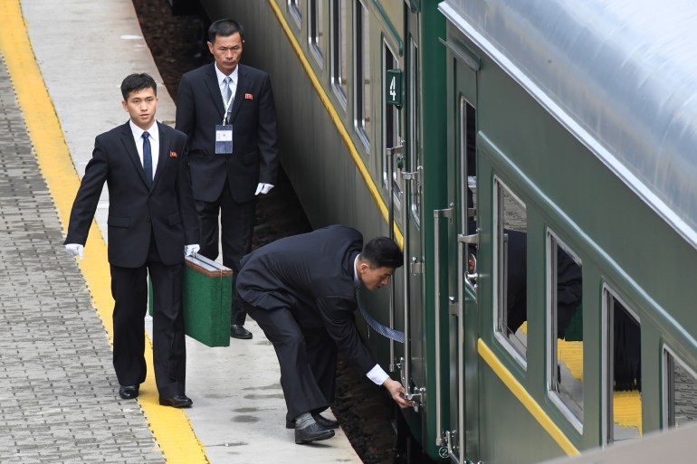 North Korean officials checking Kim's train prior to departure. There are three of them. One is carrying a large green bag, and one bending down to adjust something at the bottom of the door