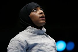 Ibtihaj Muhammad looks up while wearing a hijab and fencing gear
