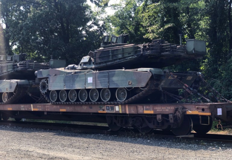 An M1 Abrams tank sits atop a flat car in a rail yard after U.S