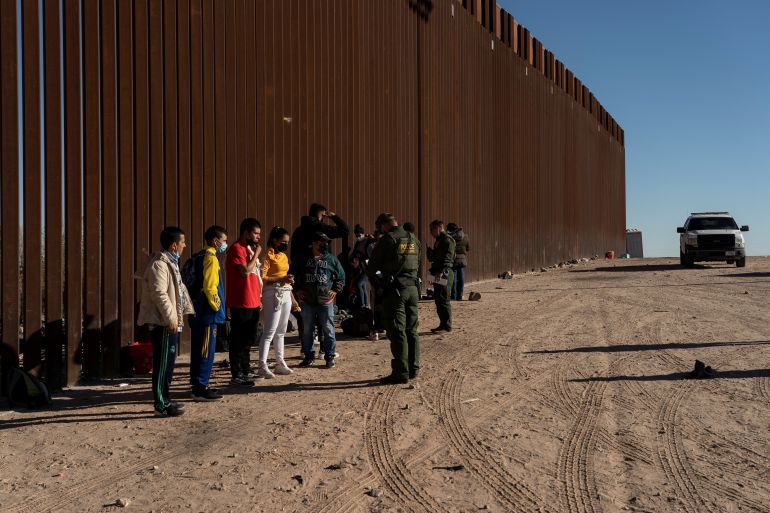 Migrants seeking asylum in the US stand in front of the border wall with Mexico, in Arizona