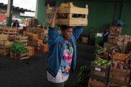 A Brazilian woman carries a box of fruit and vegetables donated by merchants at the CEASA supply centre in Rio de Janeiro, on August 30, 2022 [File: Reuters/Pilar Olivares]