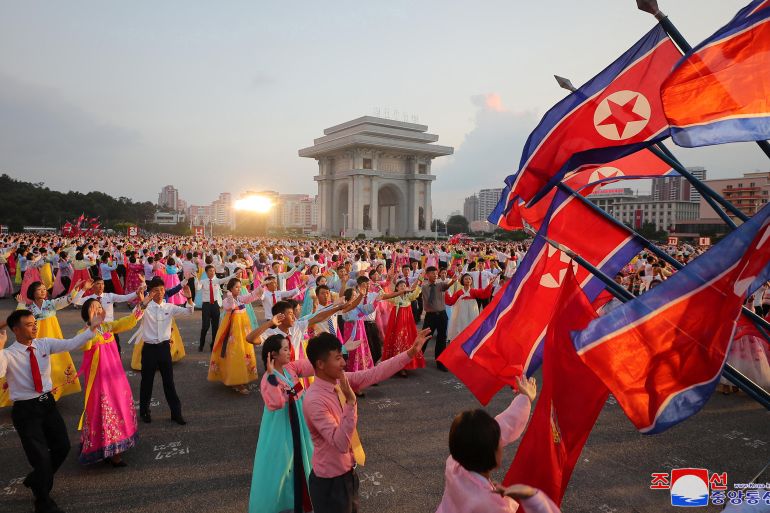 North Korean flags flying in Pyongyang at an outdoor party to mark the end of Japanese colonial rule. Many of the revellers are wearing traditional Korean clothing.
