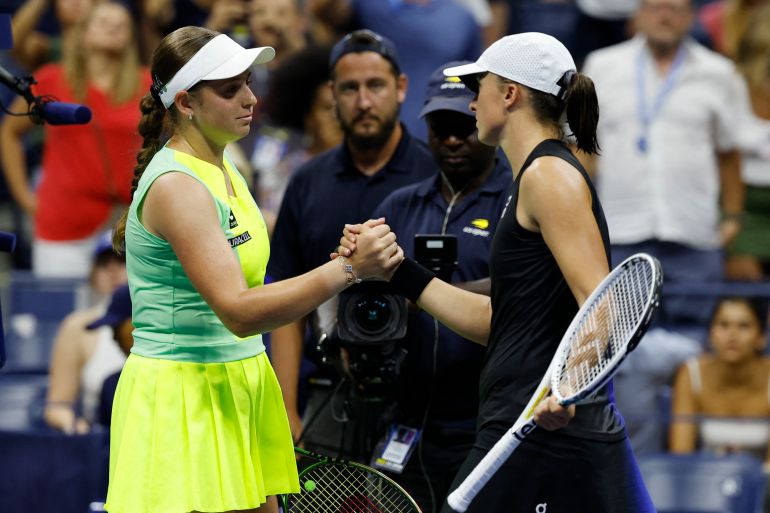 Jelena Ostapenko of Latvia (L) shakes hands with Iga Swiatek of Poland (R) after their match at the US Open. Ostapenko is wearing lime green and Swiatek navy blue. They look serious.