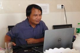 Myanmar photojournalist Sai Zaw Thaike is seen working at his laptop. He is sitting at a desk.
