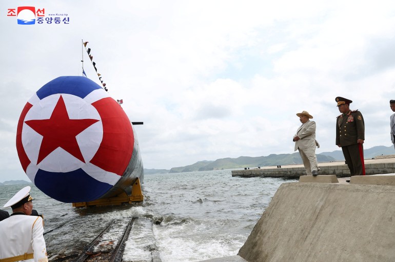 The submarine slips into the water. Kim Jong Un is standing on the dock watching.