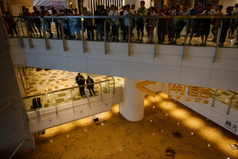 People crowded onto an upper floor walkway of a shopping centre as the floor below them floods
