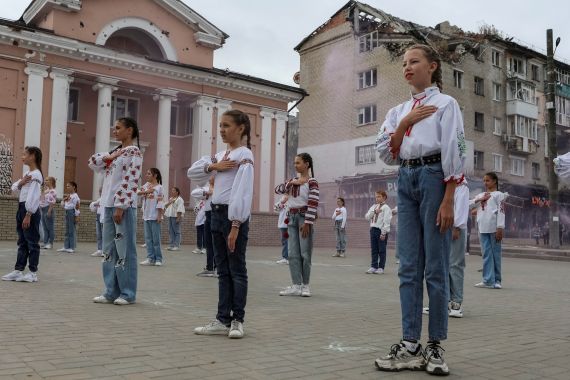 Ukrainian children standing in a square in Izyum with their hands on their hearts at an event to mark the first anniversary of the city's liberation from Russian control. They are wearing traditional shirts.