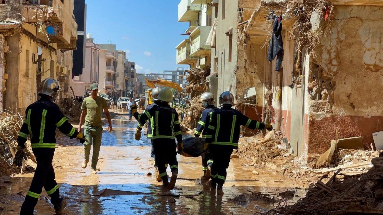 Members of the rescue teams from the Egyptian army carry a dead body as they walk in the mud between the destroyed building in Derna, Libya