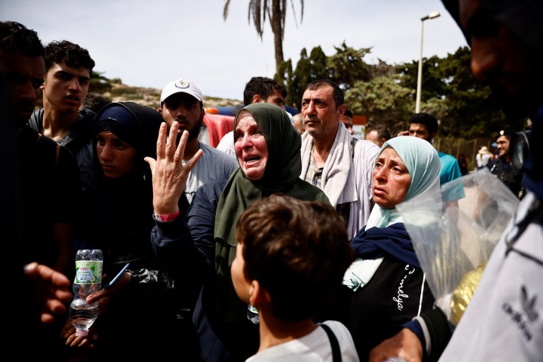 A woman cries as migrants stand outside the hotspot