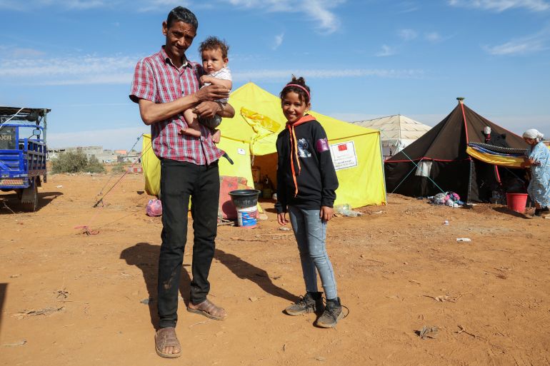 Jamal ait Khaki holds his son Walid and stands next to his daughter Fatim Zahra, 11-year-old, outside their tent, in Regraga camp