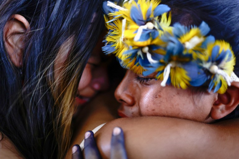 Two people, one wearing a crown of yellow and blue feathers, embrace tightly in celebration.