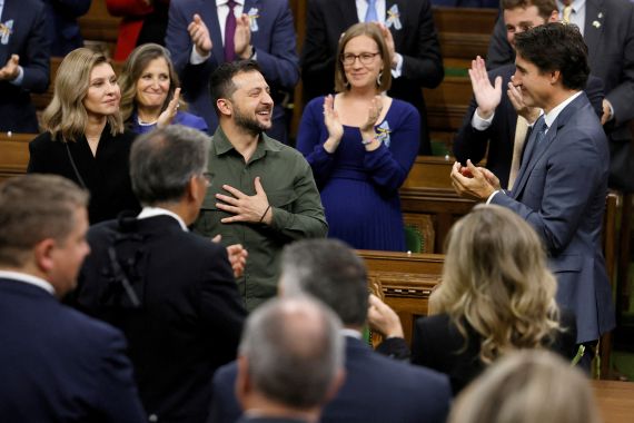 Volodymyr Zelenskyy puts a hand over his heart and smiles as Justin Trudeau and members of Canada's Parliament applaud him on the floor of the House of Commons.