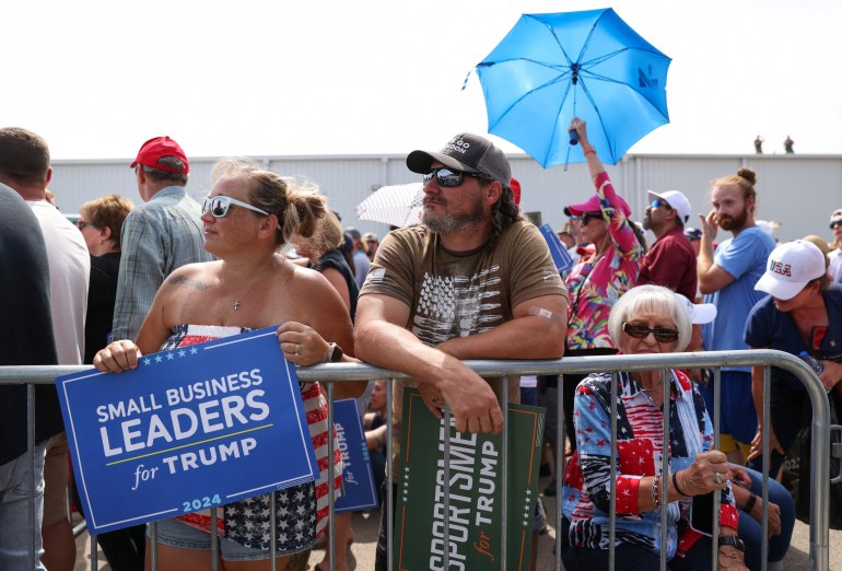 Supporters wait for former U.S. President and Republican presidential candidate Donald Trump during a 2024 presidential election campaign event at Sportsman Boats in Summerville, South Carolina, U.S. September 25, 2023.  One person holds an umbrella. Another holds a sign that reads, "Small business leaders for Trump." Others lean against a railing to hold back the crowds.