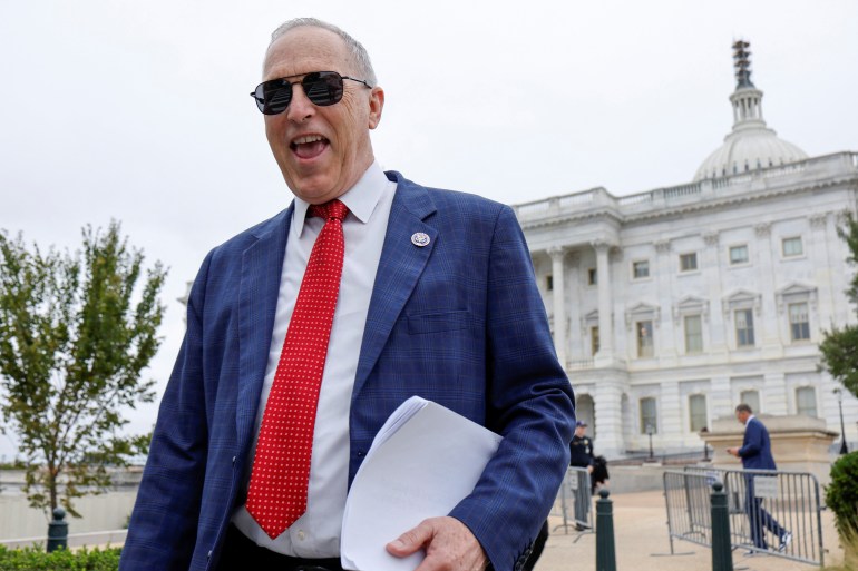 U.S. Representative Andy Biggs (R-AZ) laughs at another House member's quip as they depart after a vote at the U.S. Capitol ahead of a looming government shutdown in Washington, U.S. September 29, 2023. He wears sunglasses and is caught in mid-laugh, the Capitol building seen behind him.