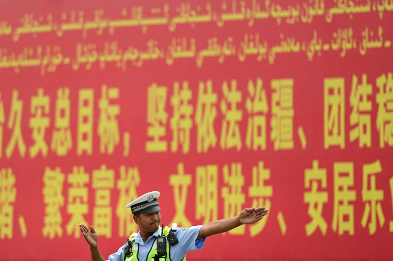 Sincan'da trafiği yöneten bir polis memuru.  Arkasındaki kırmızı reklam panosu bölgede hukukun üstünlüğünü korumanın gerekliliğini ilan ediyor.  Sözcükler sarı renkle Uygur alfabesiyle ve Çince karakterlerle yazılmıştır.