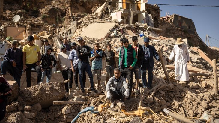 People stand in the rubble of collapsed houses in the village