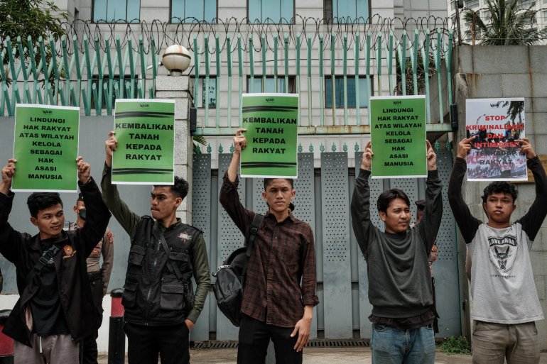 Environmental activists outside the Chinese embassy in Jakarta. They are standing in a row facing the camera and each holding a sign, urging the government to respect human rights, and return the land to the people.