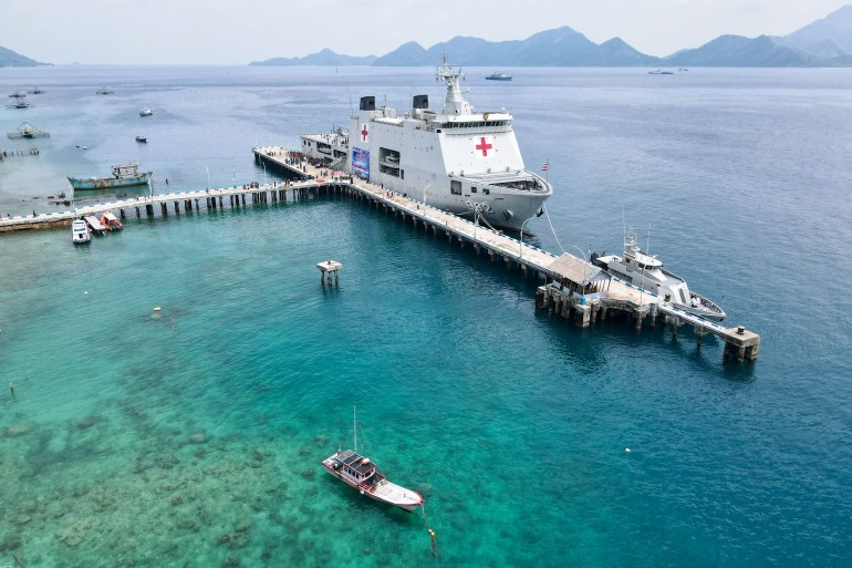 An aerial view of the Indonesian hospital ship docked off Lagong Island. The ship has a red cross on the bridge. There are other islands behind. The water is turquoise and clear