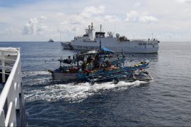 A Philippine fishing boat sails past a Chinese coastguard ship (background) near the Chinese-controlled Scarborough Shoal in disputed waters of the South China Sea [Ted Aljibe/AFP]