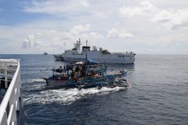 A Philippine fishing boat sails past a Chinese coastguard ship (background) near the Chinese-controlled Scarborough Shoal in disputed waters of the South China Sea [Ted Aljibe/AFP]
