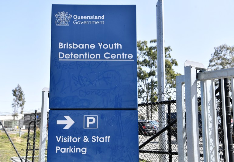 Exterior do Centro de Detenção Juvenil de Brisbane.  É uma grande placa azul perto de uma cerca