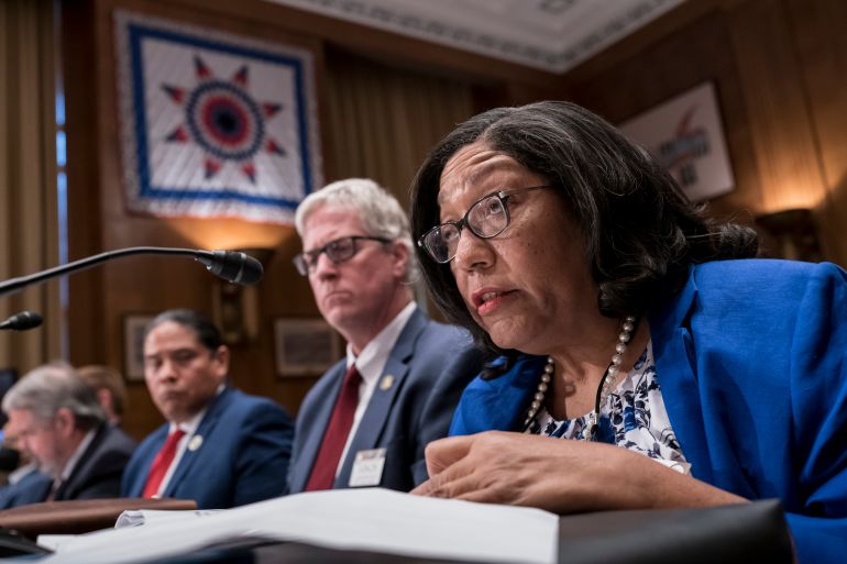 Marilyn Vann speaks into a microphone, with papers in front of her. She shares a long, panel-like desk with several other people before the Senate Indian Affairs Committee